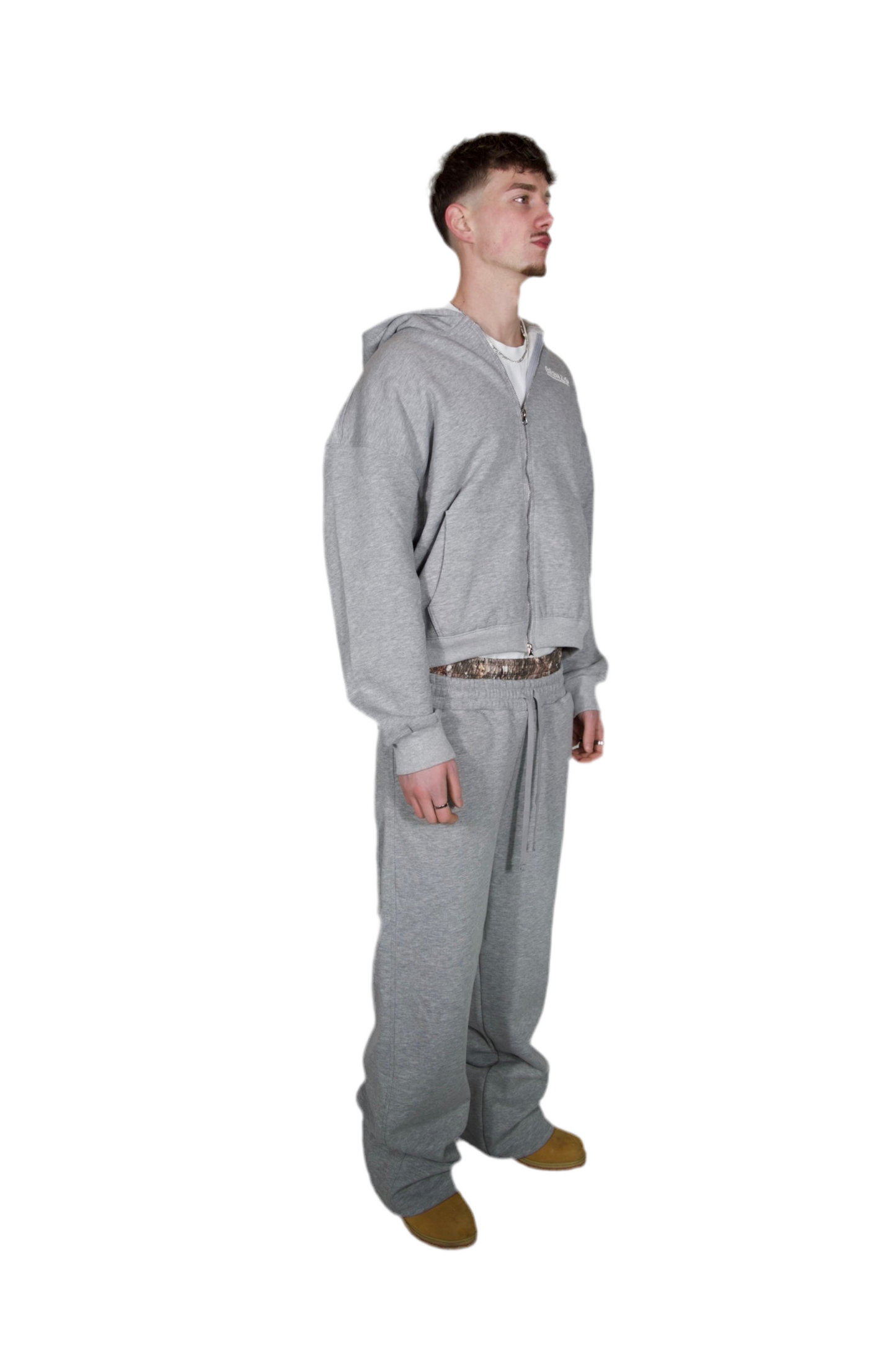 A man dressed in a grey hoodie and sweatpants, standing casually in a relaxed pose.