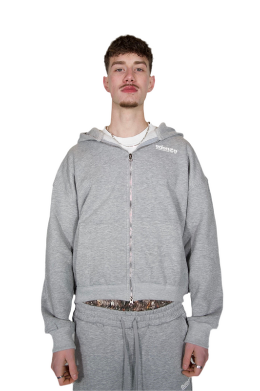 A man dressed in a grey hoodie and sweatpants, standing casually in a relaxed pose.